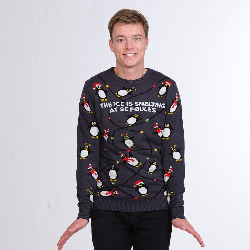 En man i en grå jultröja med pingviner och ljus.